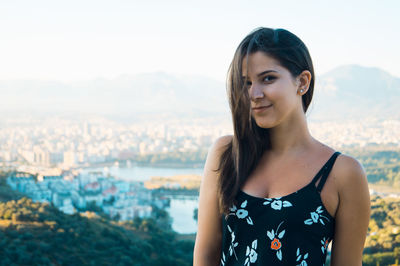 Portrait of young woman standing against cityscape