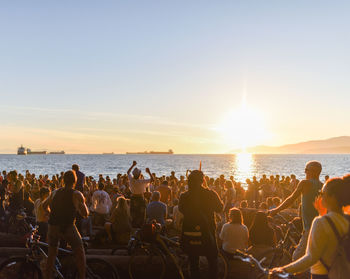 People at beach against clear sky during sunset