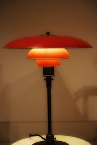 Close-up of illuminated lamp on table against wall