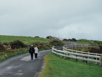 Rear view of people walking on road against sky