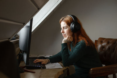 Middle age woman listening to music in big headphones near computer at home. creating play list