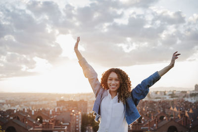 Woman with arms outstretched standing against cityscape