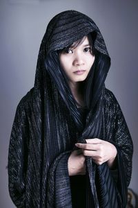 Portrait of young woman with scarf standing against gray background