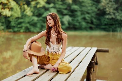Young woman sitting on pier over lake