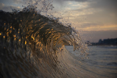 Close-up of wave splashing in sea against sky during sunset
