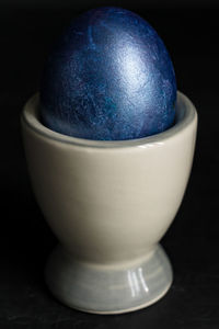 Dark blue easter egg in ceramic holder on black background. concept of minimal easter backdrop