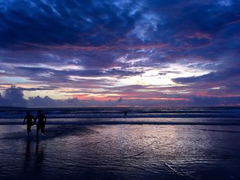Silhouette men running in sea against sky during sunset
