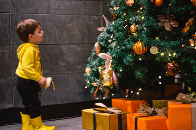 Side view of boy standing by christmas tree