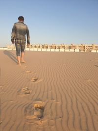 Rear view of man walking on sand at beach against clear sky