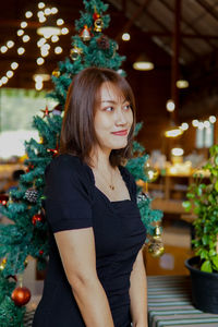 Portrait of young woman standing against christmas tree at home
