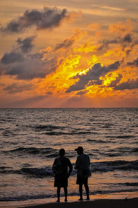 Rear view of men on beach against sky during sunset