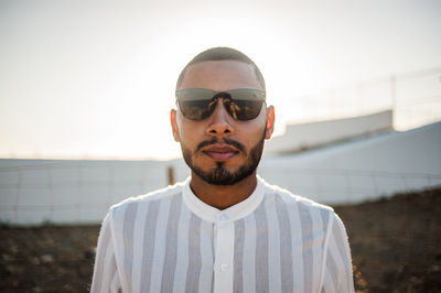 Portrait of young man wearing sunglasses standing against sky