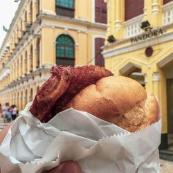 Cropped hand holding burger against building in city