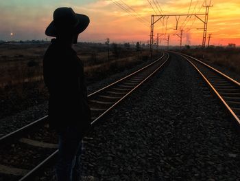 Silhouette man standing on railroad track against sky during sunset