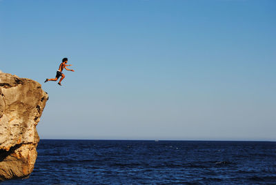 Full length of shirtless man jumping from cliff into sea
