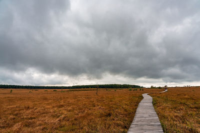 Dirt road on field against storm clouds