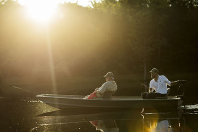 Friends sitting in rowboat while fishing at lake