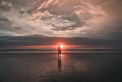 Silhouette man standing at beach against sky during sunset