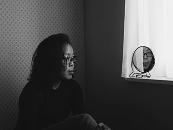 Mid adult woman looking at mirror while sitting in bedroom at home