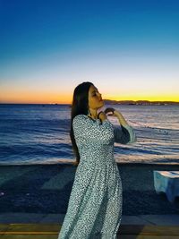 Woman standing at beach against sky during sunset