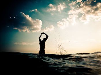 Silhouette person in sea against sky during sunset