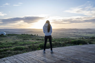 Woman contemplating the view while standing on a wooden deck at sunset.