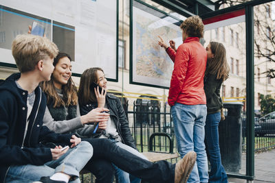 Male and female friends waiting at bus stop in city