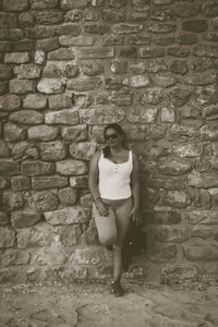 Portrait of young woman standing against brick wall