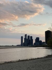 Sea by buildings against sky during sunset