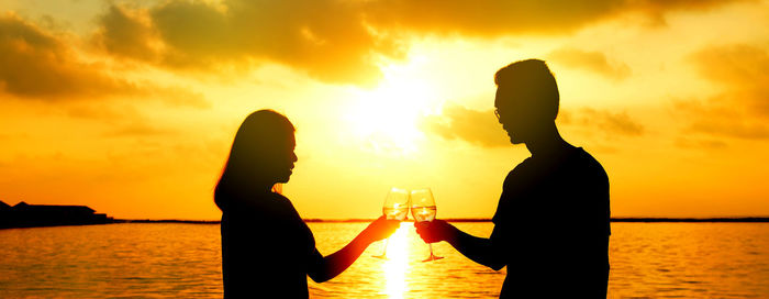 Silhouette couple toasting drink at beach during sunset