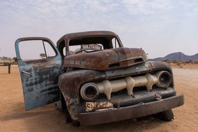 Abandoned vintage car on land against sky
