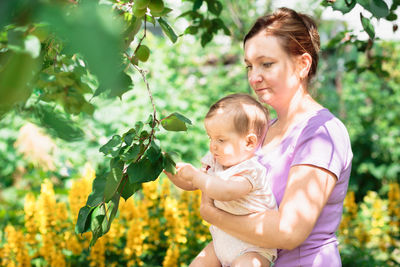 Woman with daughter standing by plants in yard