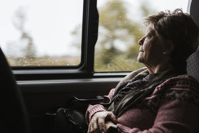 Thoughtful senior woman looking through car window