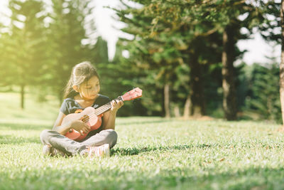 Girl playing guitar on field against trees