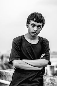 Portrait of young man with arms crossed standing against sky