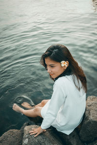 High angle view of young woman sitting on rock by lake