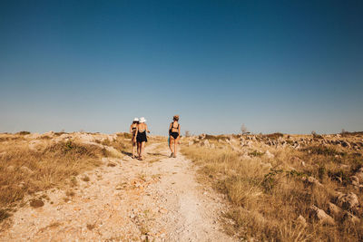 Rear view of people walking on field against clear sky