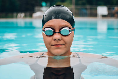 Portrait of smiling young woman wearing swimming goggles and cap in pool