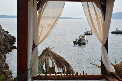 View on a calm sea surface with boats from a cabana bed with white curtain