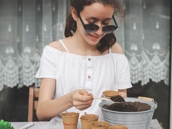 Caucasian teenage girl in sunglasses  fills the soil with a wooden spoon into a cardboard glass