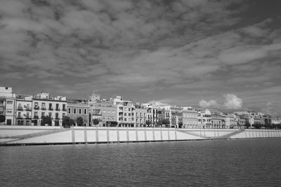 View of buildings by river against cloudy sky