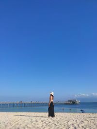 Rear view of woman standing at beach against clear blue sky