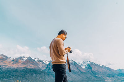 Man holding camera while standing on land against mountains and sky
