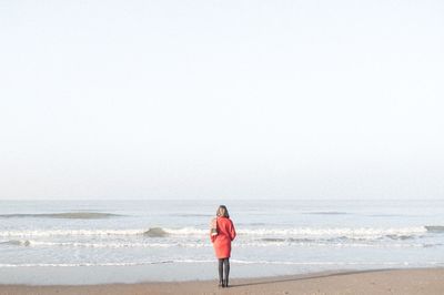 Rear view of woman standing on beach against clear sky