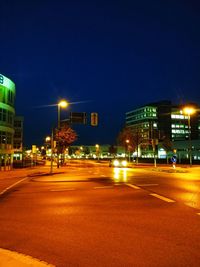 Illuminated street by buildings against clear sky at night