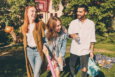 Cheerful young friends enjoying picnic while standing at back yard during summer