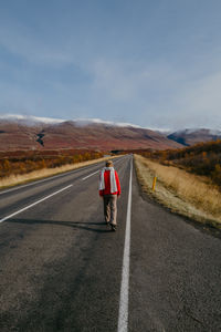 Woman in a red jumper and a scarf walking on the road in iceland