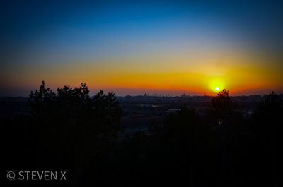 Silhouette trees and cityscape against sky during sunset