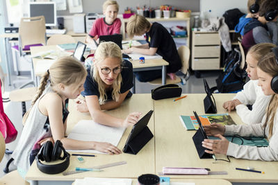 Teacher assisting high school girl using digital tablet in classroom