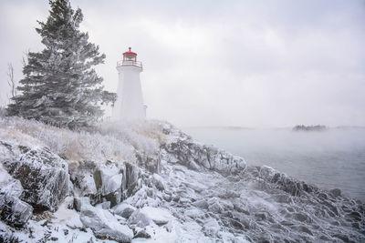 Lighthouse by sea against sky during winter